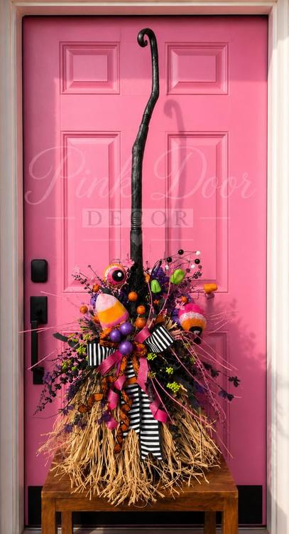 Decorated witch’s broom with candy corn and striped bows in front of the pink door